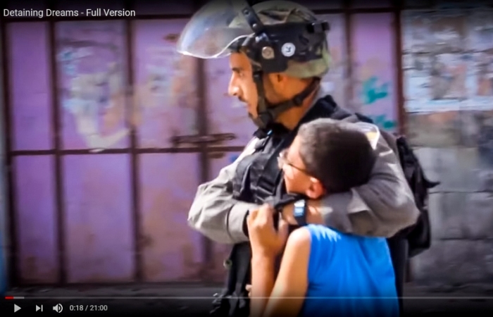 An Israeli soldier walks with his arms around the shoulders and neck area of a struggling Palestinian boy - screenshot from the short documentary Detaining Dreams.