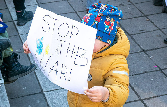 A young child holds up a sign reading "Stop the war!" with the colours of the Ukraine flag. 