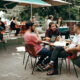 Three men sit around a table at an outdoor cafe having a conversation and listening to each other.