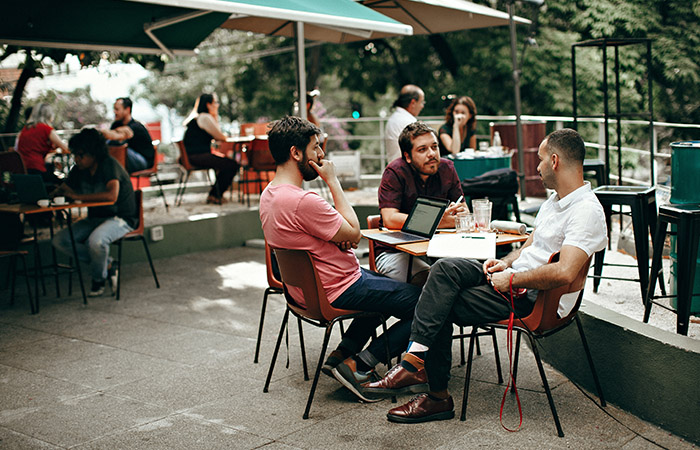 Three men sit around a table at an outdoor cafe having a conversation and listening to each other.