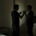 A man in a dark room shouts at himself in the mirror