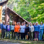 CFSC Members and staff stand outdoors in front of a wooden building