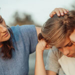 A mother pats the head of her adolescent son, who seems upset