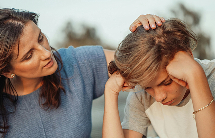 A mother pats the head of her adolescent son, who seems upset
